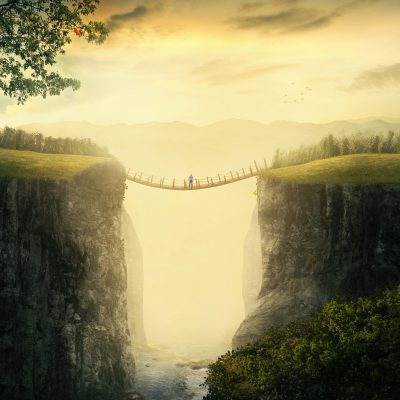 A man stands alone on a bridge between two mountains.